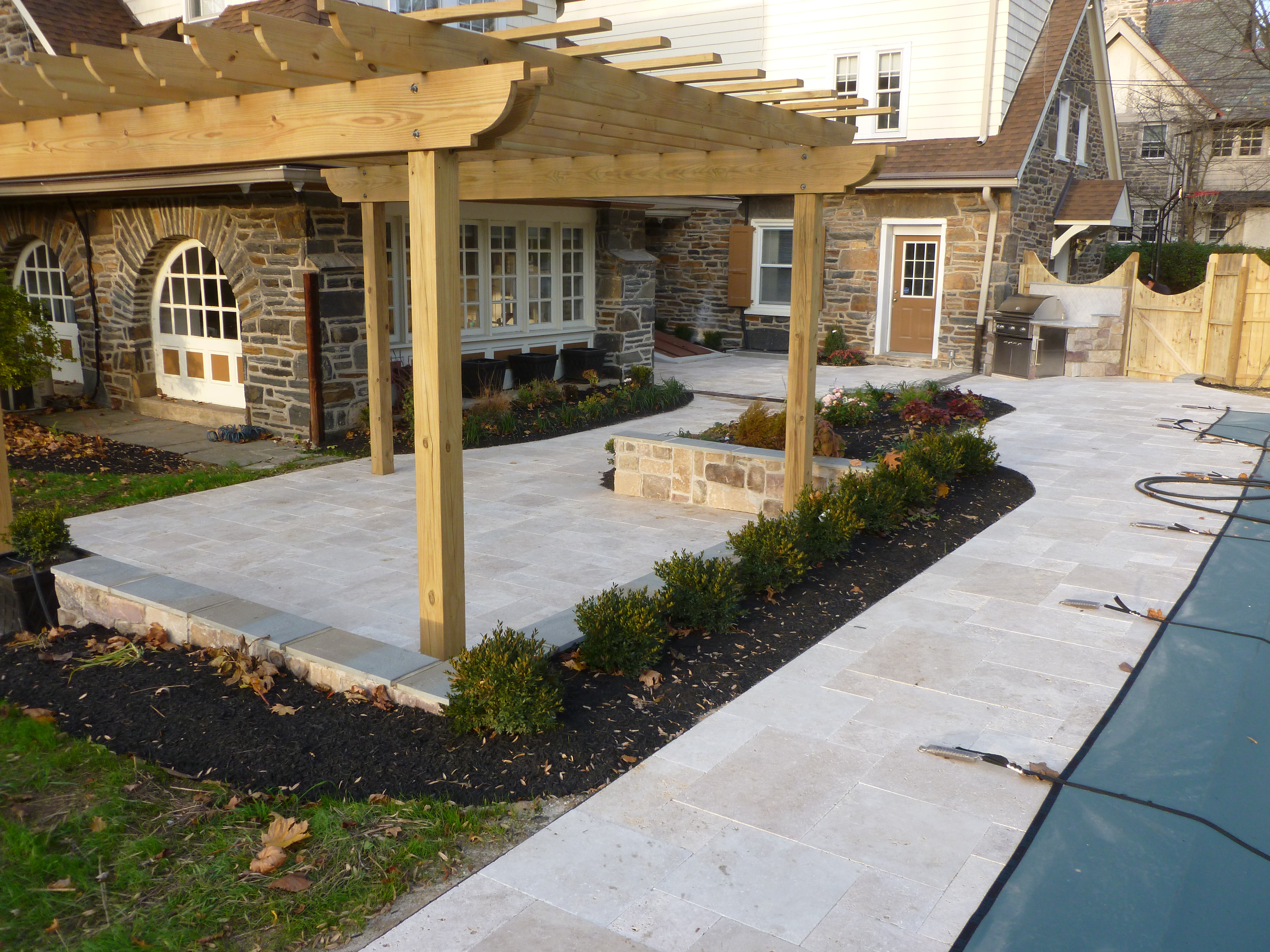 The final project featured a hardscaped patio and walls covered with Travertine pavers on all surfaces including the pool surround and a custom built pergola. (Image via aardweglandscaping.com – Main Line Philadelphia PA)